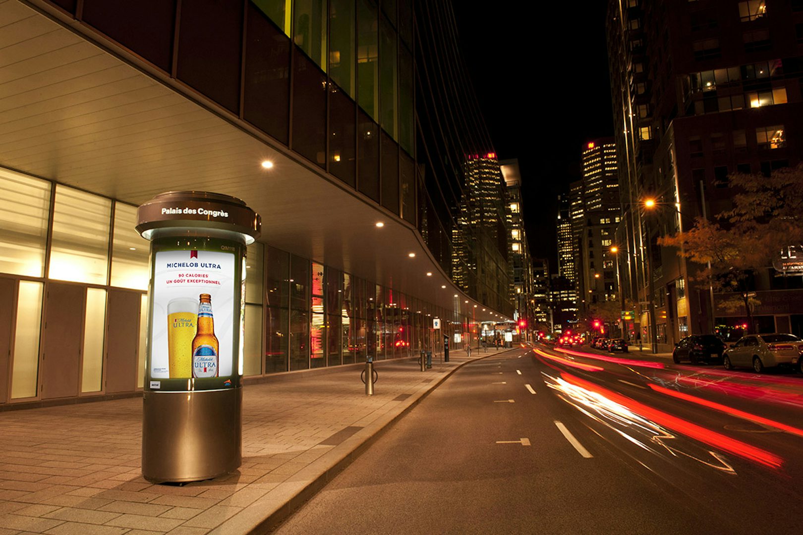 Astral street column alongside a busy street at night featuring a Michelob Ultra ad