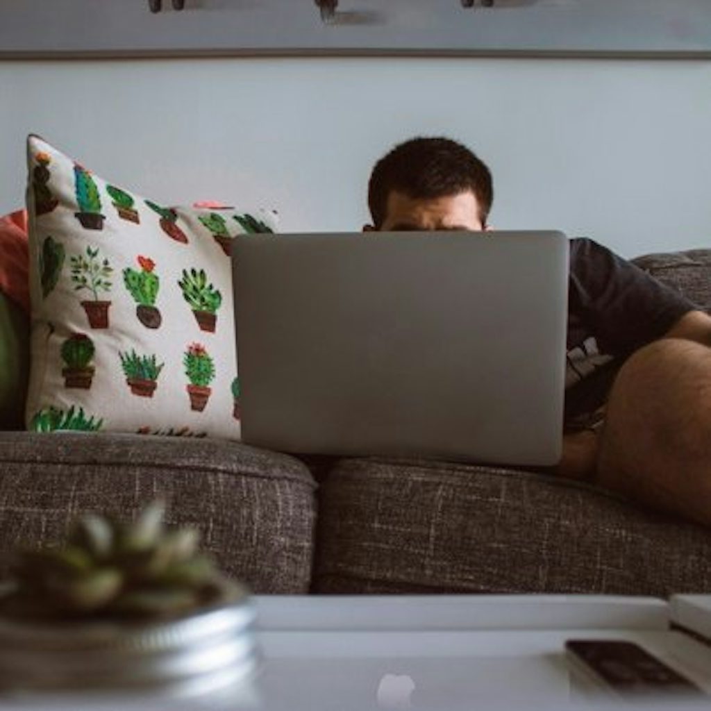 Man sitting on couch covered by a laptop