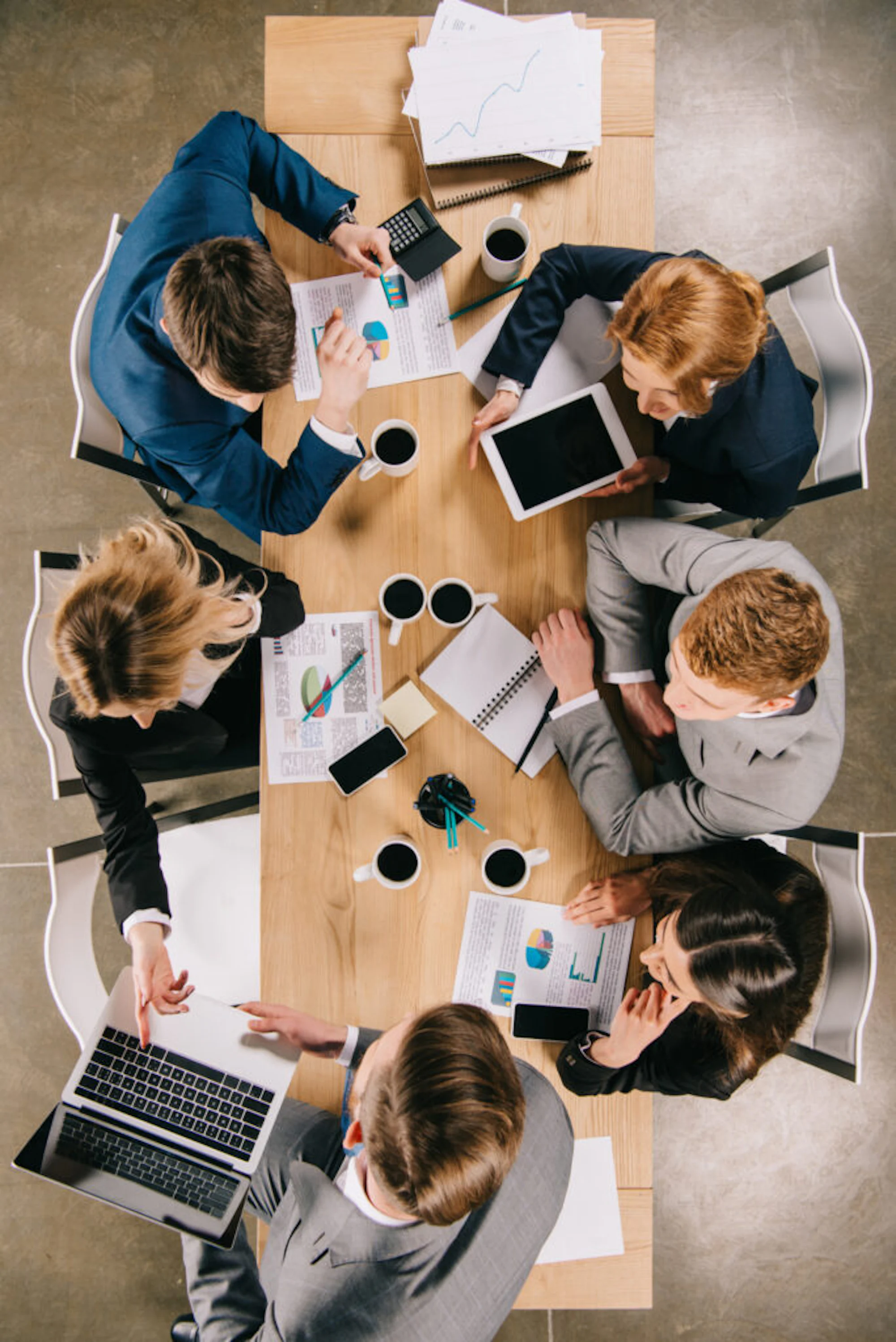 overhead view of businessman showing presentation to partners at table with digital devices, coffee cups and documents
