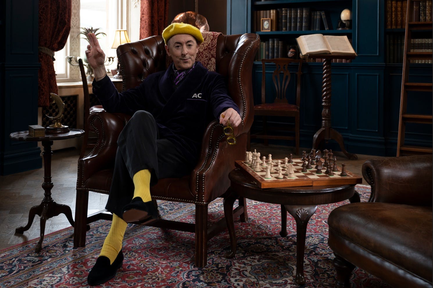 Alan Cumming sits in a chair beside a chess game in the series premiere of THE TRAITORS: US