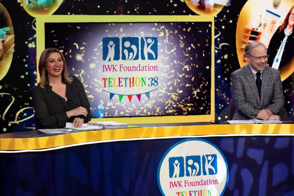 IWK Telethon Hosts Maria Panopalis and Todd Battis sitting at desk on set of Telethon