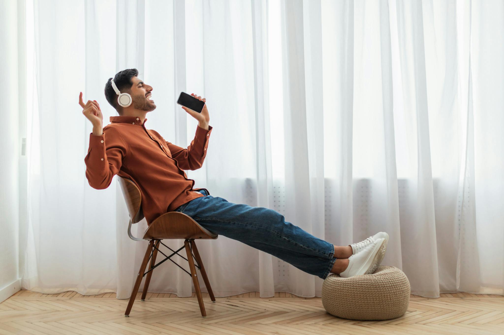 Cheerful young guy listening to radio using cell phone and wearing wireless headset.