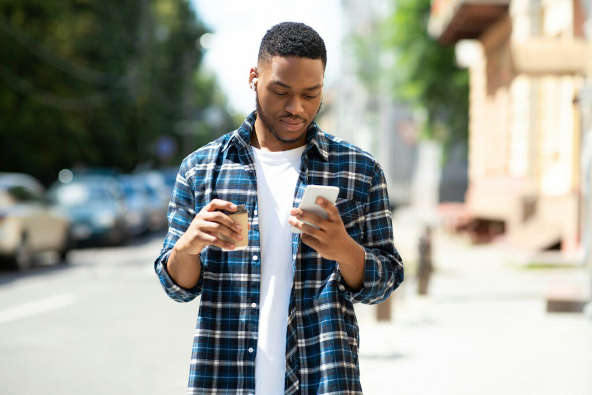 young black hipster listening to music on his cell phone, walking down the street with coffee cup