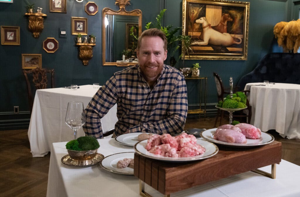 Jon Montgomery sitting on a breakfast table with dishes of raw pig brains and bison testicles in front of him.