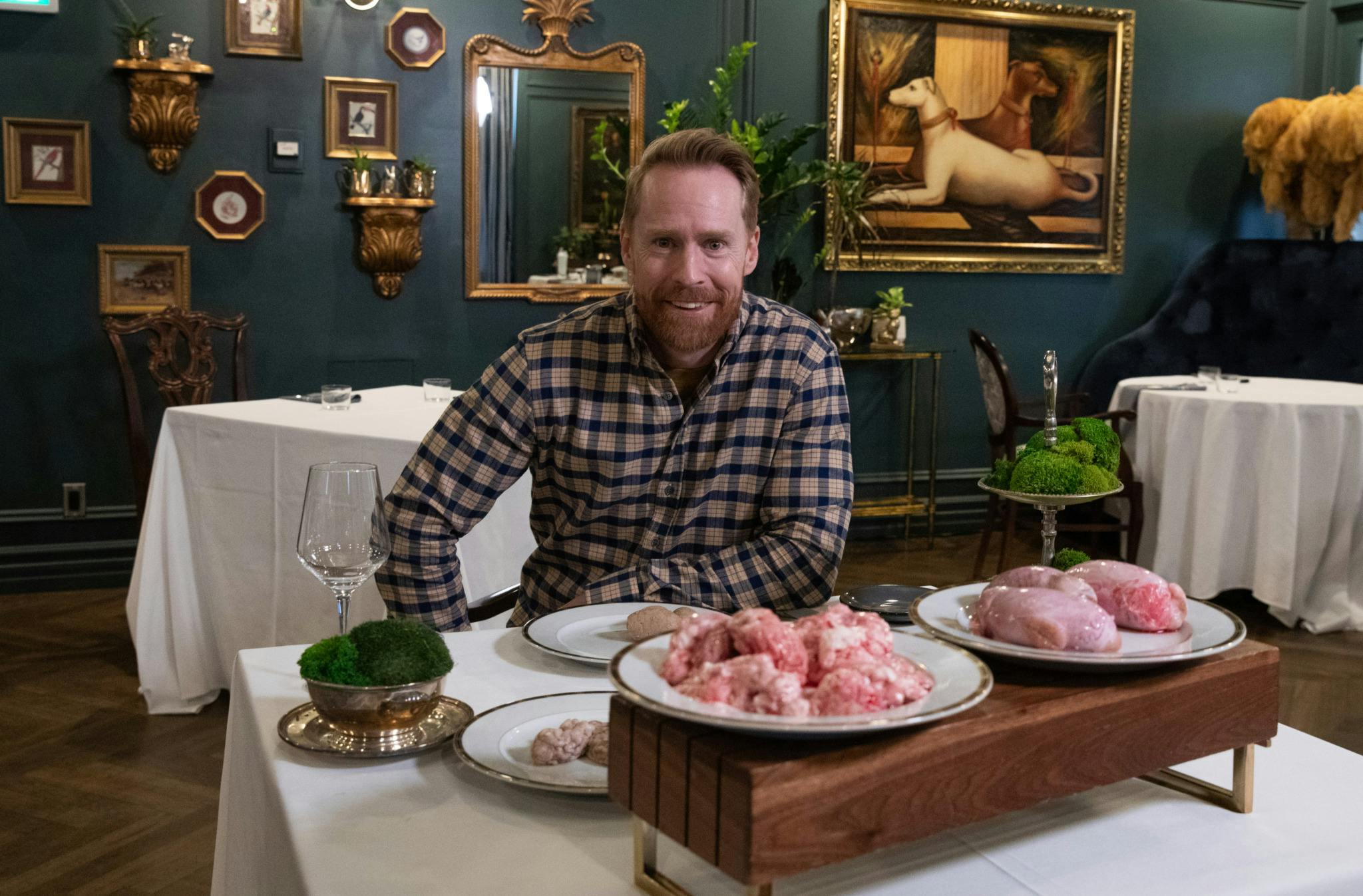 Jon Montgomery sitting on a breakfast table with dishes of raw pig brains and bison testicles in front of him.