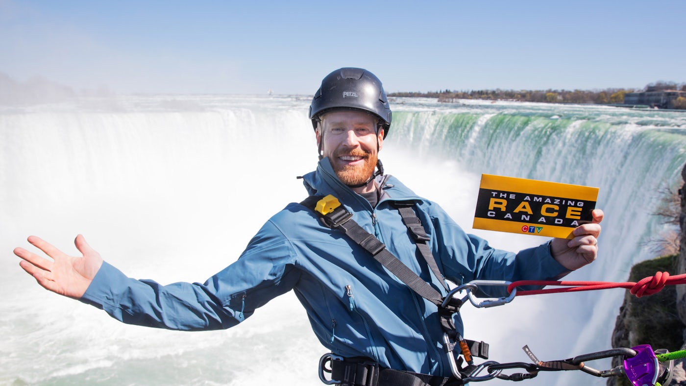 Jon Montgomery hanging in front of Niagara Falls holding a sign.