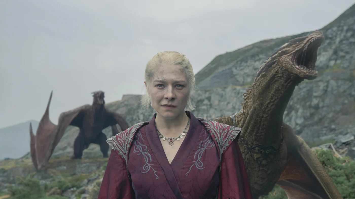 Rhaenyra Targaryen standing in front of two dragons on a mountain.