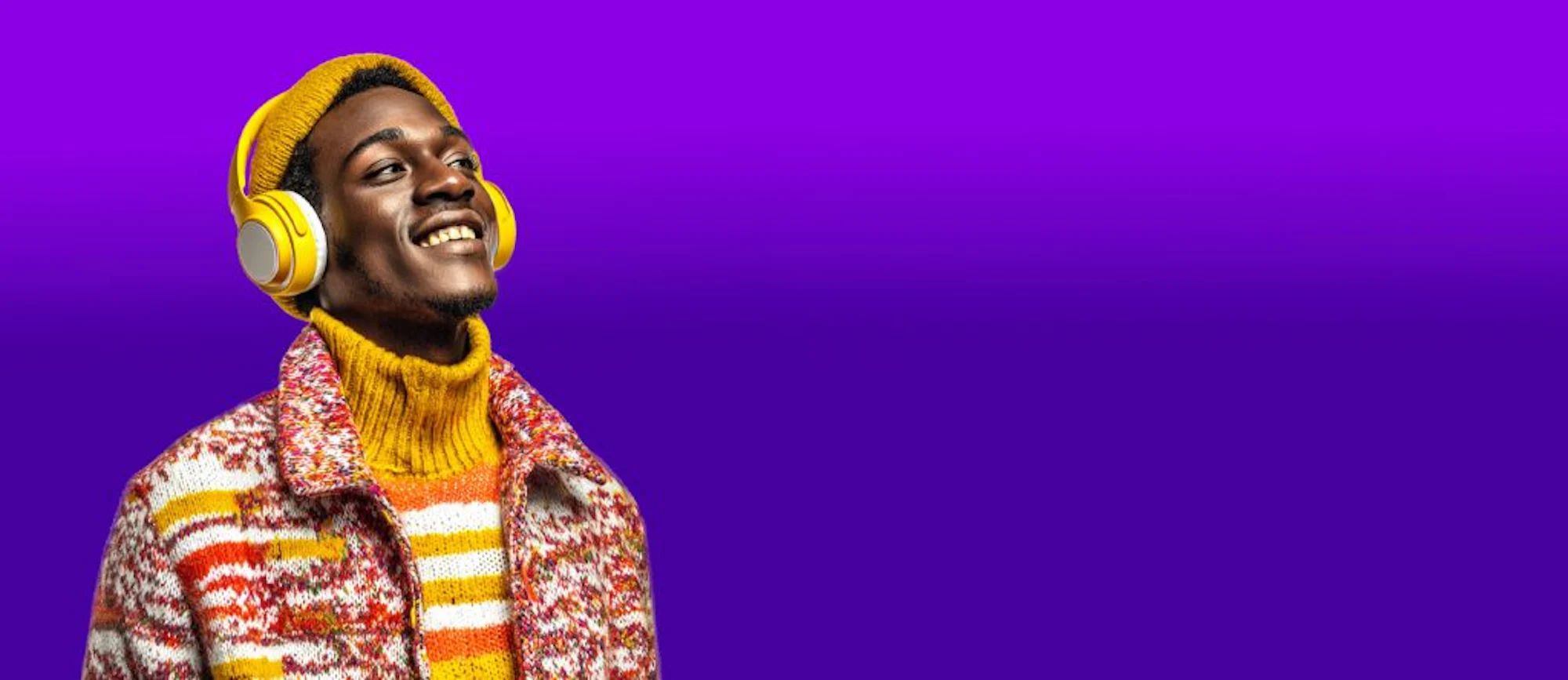 Young man smiling while listening to music with headphones against a purple background